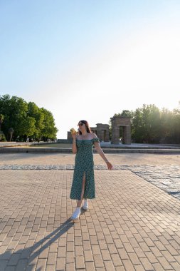 Genç bir kadın yazın Madrid, İspanya 'daki debod tapınağının önünde akıllı telefon kullanıyor, yürüyor ve sesli mesaj kaydediyor.