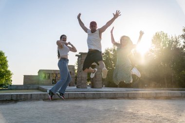 Üç arkadaş yaz günbatımının tadını çıkarıyorlar. Madrid, İspanya 'daki eski Mısır temposunun önünde sevinçten zıplıyorlar.