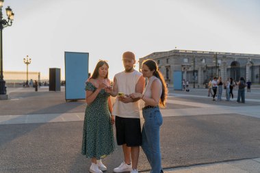 Yaz tatilinde gün batımında Madrid Kraliyet Sarayı 'nın yakınındaki bir akıllı telefona danışan üç arkadaş.