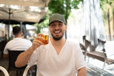 Kafkasyalı genç adam güneşli bir yaz gününde kaldırım kafesinde serinletici bir bira içiyor.