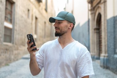 Bir yaz tatili boyunca büyüleyici bir Avrupa şehrini keşfederken şapkalı ve akıllı telefonunun keyfini çıkaran genç bir adam.