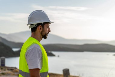 Güvenlik kaskı ve yelek giyen mühendis doğal ortamda su kaynaklarını ve yenilenebilir enerji üretimini denetliyor.