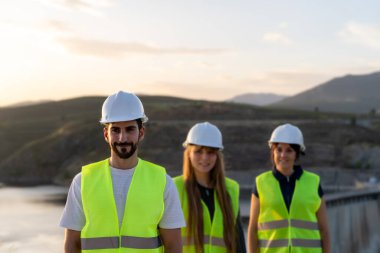 Gün batımında barajın yanında çalışan güvenlik kaskı ve yelekleri takan bir grup mühendis inşaat görevlerine odaklandı.