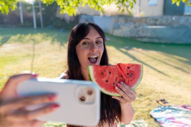 Yazın parkta bir dilim karpuz yerken fotoğraflanan bir kadın komik bir yüz ifadesi takındı.