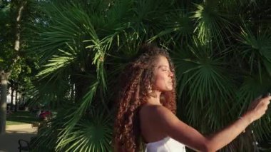 Sosyal medya içeriğini aksiyon kamerasıyla oluşturan genç bir kadın neşeli enerji ve şık varlığıyla güneşli Madrid parkında seyahat anlarını yakalıyor.