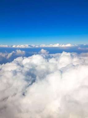Derin, berrak bir mavi gökyüzünün altında yoğun, tüylü beyaz bulutların havadan görünüşü. Bulutlar ve gökyüzü arasında açık bir ufuk çizgisi.