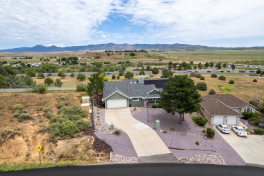 Geniş açıdan bakıldığında, ağaçların arasına yerleştirilmiş birkaç evi olan sakin bir yerleşim yeri görülüyor. Gündüz vakti, açık mavi gökyüzünün altındaki açık arazi ve tepeleri de kapsıyor..
