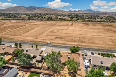 Geniş açıdan bakıldığında, ağaçların arasına yerleştirilmiş birkaç evi olan sakin bir yerleşim yeri görülüyor. Gündüz vakti, açık mavi gökyüzünün altındaki açık arazi ve tepeleri de kapsıyor..