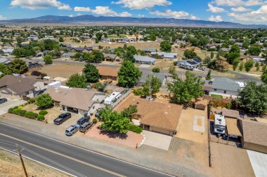 Geniş açıdan bakıldığında, ağaçların arasına yerleştirilmiş birkaç evi olan sakin bir yerleşim yeri görülüyor. Gündüz vakti, açık mavi gökyüzünün altındaki açık arazi ve tepeleri de kapsıyor..