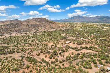 Geniş bir çöl arazisi, uzak dağlar ve yeşillik alanlarına karşı kurulur. Sahne, parlak bir gökyüzünün altında doğal güzellikleri yansıtan sakin bir atmosfer yakalıyor..