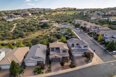 Geniş açıdan bakıldığında, ağaçların arasına yerleştirilmiş birkaç evi olan sakin bir yerleşim yeri görülüyor. Gündüz vakti, açık mavi gökyüzünün altındaki açık arazi ve tepeleri de kapsıyor..