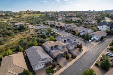 Geniş açıdan bakıldığında, ağaçların arasına yerleştirilmiş birkaç evi olan sakin bir yerleşim yeri görülüyor. Gündüz vakti, açık mavi gökyüzünün altındaki açık arazi ve tepeleri de kapsıyor..