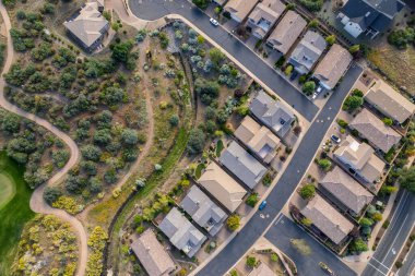 Geniş açıdan bakıldığında, ağaçların arasına yerleştirilmiş birkaç evi olan sakin bir yerleşim yeri görülüyor. Gündüz vakti, açık mavi gökyüzünün altındaki açık arazi ve tepeleri de kapsıyor..