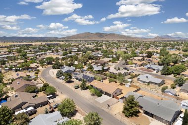 Geniş açıdan bakıldığında, ağaçların arasına yerleştirilmiş birkaç evi olan sakin bir yerleşim yeri görülüyor. Gündüz vakti, açık mavi gökyüzünün altındaki açık arazi ve tepeleri de kapsıyor..