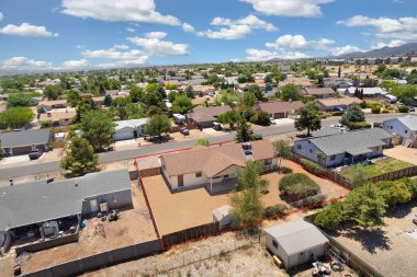 Geniş açıdan bakıldığında, ağaçların arasına yerleştirilmiş birkaç evi olan sakin bir yerleşim yeri görülüyor. Gündüz vakti, açık mavi gökyüzünün altındaki açık arazi ve tepeleri de kapsıyor..