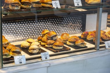 Çeşitli lezzetli hamburgerler pırıl pırıl cam bir rafta, çeşitli lezzet ve malzemeler sergiliyorlar.