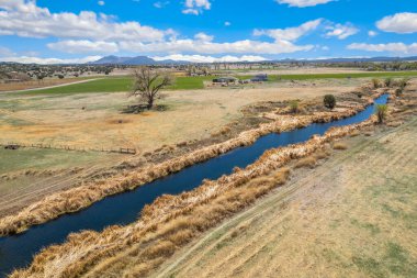 Bu çarpıcı hava manzarası, berrak mavi gökyüzünün altındaki yemyeşil çayırlarda zarafetle kıvrılan sakin bir nehri yakalar.
