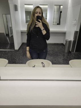 Bir kadın banyo aynasının önünde duruyor ve bu temiz ve düzenli yerde mutlu bir şekilde selfie çekiyor.