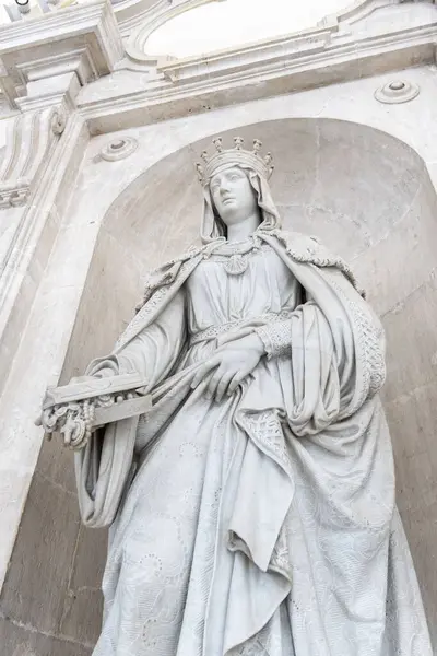 Akan beyaz bir elbise giymiş güzel bir kadın heykeli zarif bir şekilde muhteşem bir binanın önünde duruyor.