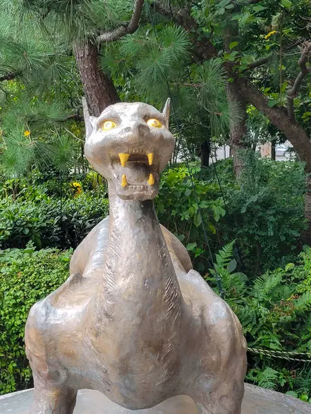Efsanevi yaratık heykeli güneşli öğleden sonra yemyeşil ve parlak çiçeklerle dolu canlı bir bahçede nöbet tutar. Yüksek kalite fotoğraf
