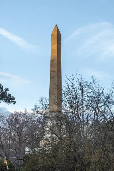 Yükselen, büyük bir dikilitaş, berrak mavi gökyüzünün altında görkemli yeşil ağaçlarla çevrili, resim gibi bir manzara yaratıyor.