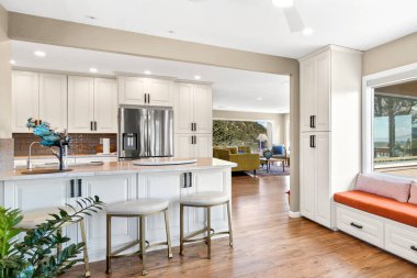 İçinde beyaz dolaplar, şık tabureler, büyük bir buzdolabı ve ek konfor ve cazibe için rahat bir pencere kenarı bulunan modern bir mutfak.