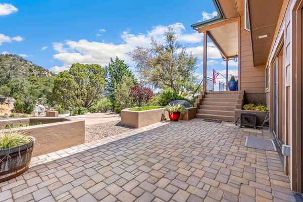 A spacious and large brick patio area positioned right in front of a house featuring a welcoming porch and steps that lead up to it