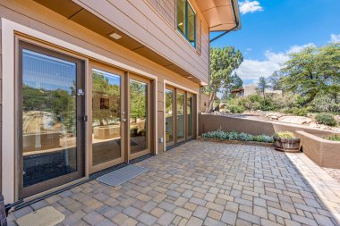 Geniş ve büyük bir tuğla avlu. Tam bir evin önünde. Hoş geldin verandası ve ona doğru giden merdivenler var.