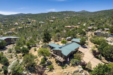 Geniş bir hava manzarası, bereketli ağaçların ve görkemli dağların arasına yerleşmiş sakin bir ev sergiliyor.