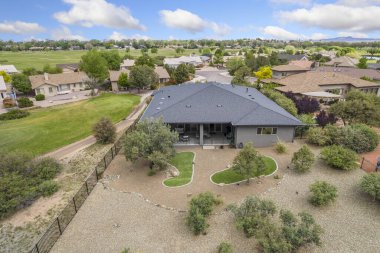 Bu resim, bereketli ağaçlar ve canlı otlar tarafından kucaklanan huzurlu bir yerleşim alanına yerleştirilmiş resimli bir evin havadan görüntüsünü sergiliyor.