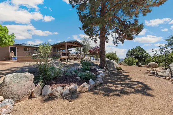 Geniş bir hava manzarası, bereketli ağaçların ve görkemli dağların arasına yerleşmiş sakin bir ev sergiliyor.