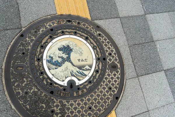 Tokyo, Japonya - 5 Ocak 2025: Japonya 'da tarihi sanat eserleri keşfedilmesi çarpıcı bir dalga tasarımı ortaya çıkararak, dolup taşan bir kaldırım boyunca bir rögar kapağı süsledi. Yüksek kalite fotoğraf