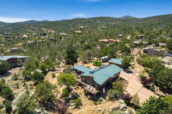 Geniş bir hava manzarası, bereketli ağaçların ve görkemli dağların arasına yerleşmiş sakin bir ev sergiliyor.