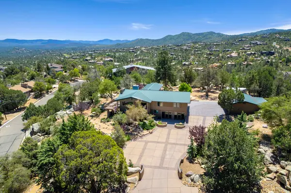 Geniş bir hava manzarası, bereketli ağaçların ve görkemli dağların arasına yerleşmiş sakin bir ev sergiliyor.