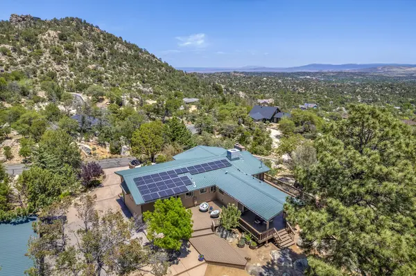 Geniş bir hava manzarası, bereketli ağaçların ve görkemli dağların arasına yerleşmiş sakin bir ev sergiliyor.