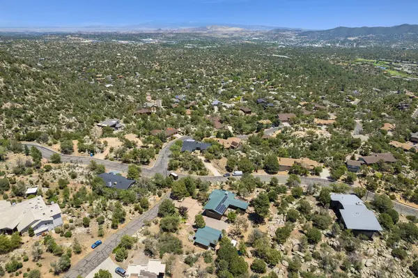 Geniş bir hava manzarası, bereketli ağaçların ve görkemli dağların arasına yerleşmiş sakin bir ev sergiliyor.
