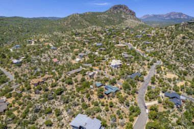 Geniş bir hava manzarası, bereketli ağaçların ve görkemli dağların arasına yerleşmiş sakin bir ev sergiliyor.