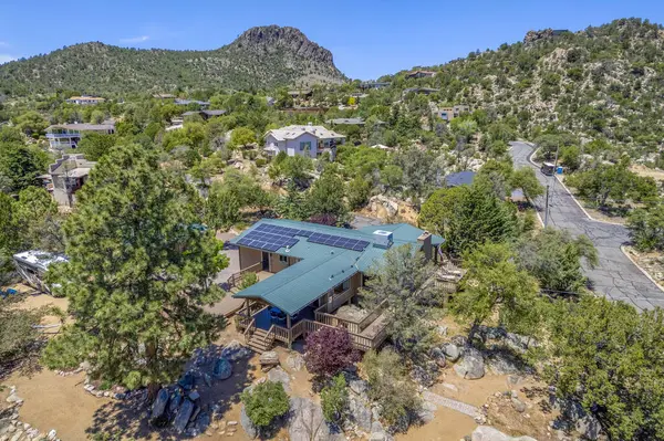 Geniş bir hava manzarası, bereketli ağaçların ve görkemli dağların arasına yerleşmiş sakin bir ev sergiliyor.