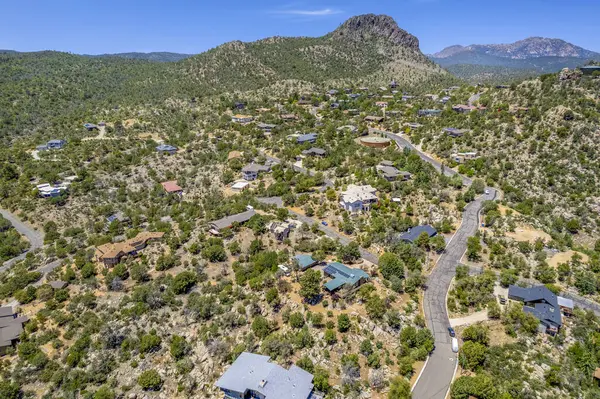 Geniş bir hava manzarası, bereketli ağaçların ve görkemli dağların arasına yerleşmiş sakin bir ev sergiliyor.