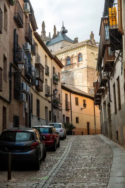 Dar, dolambaçlı bir kaldırım taşı caddesi. Arabalar yan tarafa park edilmiş. Olay yerine büyüleyici bir şehir atmosferi yaratıyor.