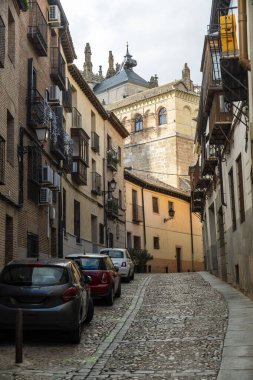 Dar, dolambaçlı bir kaldırım taşı caddesi. Arabalar yan tarafa park edilmiş. Olay yerine büyüleyici bir şehir atmosferi yaratıyor.