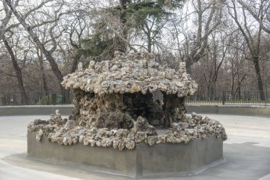 Güzel bir parkın ortasında, arkasında durgun bir zemin oluşturan uzun, yeşil ağaçlarla çevrili çarpıcı bir heykel duruyor.