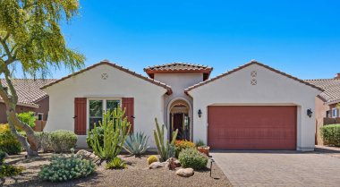 Çarpıcı kırmızı garaj kapısı olan geleneksel bir beyaz ev arka plandaki geniş mavi gökyüzüne karşı güzel bir şekilde öne çıkıyor.