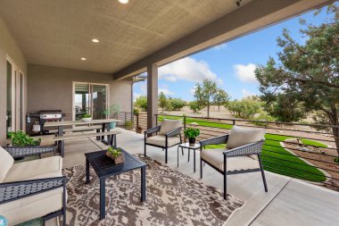 Rahat bir halı, şık sandalyeler, fonksiyonel masalar ve lezzetli yemekler pişirmek için bir ızgaranın bulunduğu güzel bir bahçe alanı.