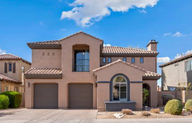 Arka planda görülebilen güzel mavi bir gökyüzünün altında iki ferah garajı olan büyük, etkileyici bir ev.