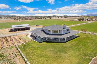 Etrafını çevreleyen geniş, yeşil çimenli bir arazinin tam ortasında güzel bir evi gösteren bir hava manzarası.