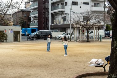 Tokyo, Japonya - 5 Ocak 2025: İki arkadaş, Japonya 'da sakin bir parkta, kış gününün ışıltısının ortasında neşeli bir öğleden sonranın tadını çıkarıyorlar. Yüksek kalite fotoğraf