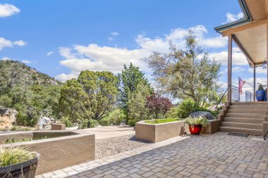 Geniş ve büyük bir tuğla avlu. Tam bir evin önünde. Hoş geldin verandası ve ona doğru giden merdivenler var.