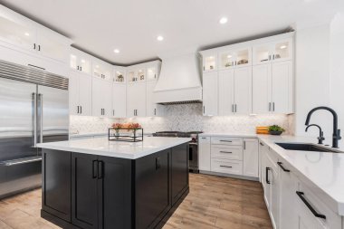 Bu zarif tasarlanmış mutfak beyaz ve siyah dolaplar, modern paslanmaz çelik aletler ve yemek hazırlamak için merkezi bir ada içerir.