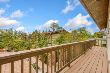 Sağlam bir korkuluk içeren davetkar ahşap bir güverte, bereketli ağaçlarla çevrili büyüleyici bir evin manzarasını sunuyor.